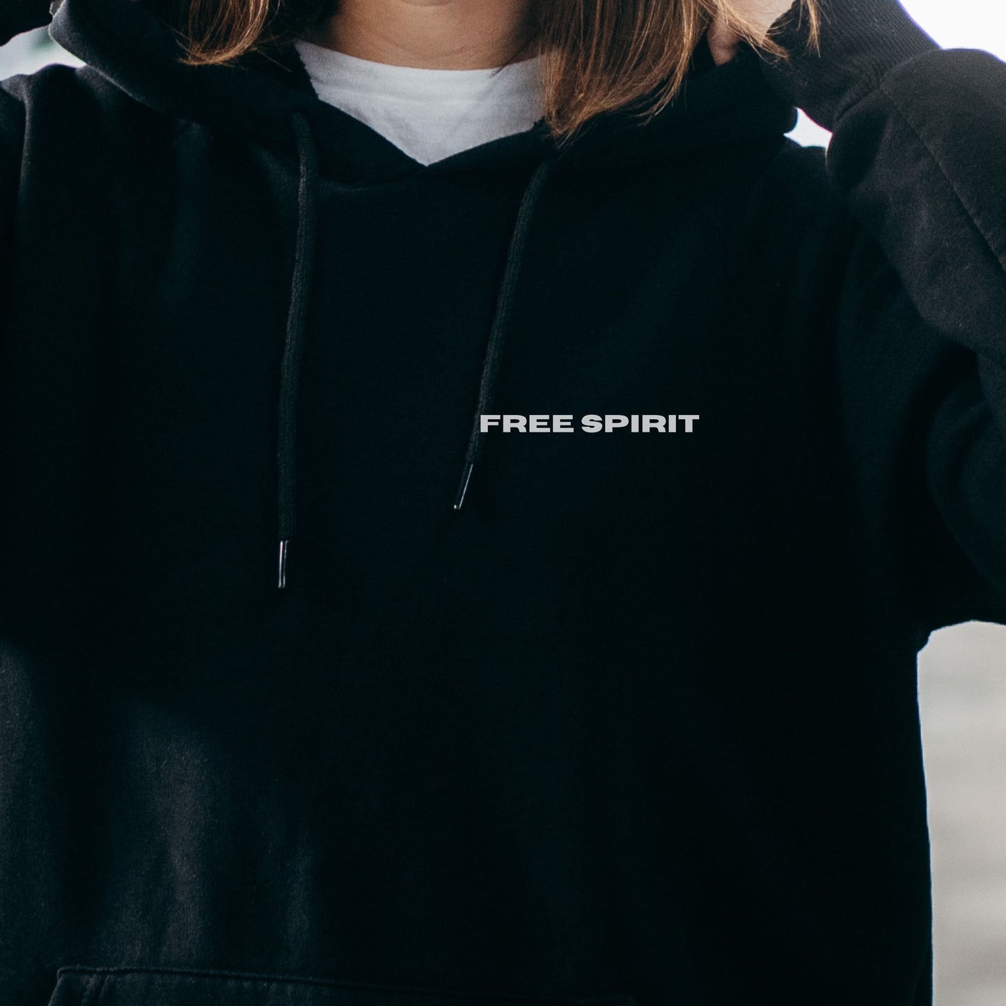 Close-up of model wearing black oversized VIKA&EVE FREE SPIRIT hoodie by the water – minimalist unisex design for who we strive to be.