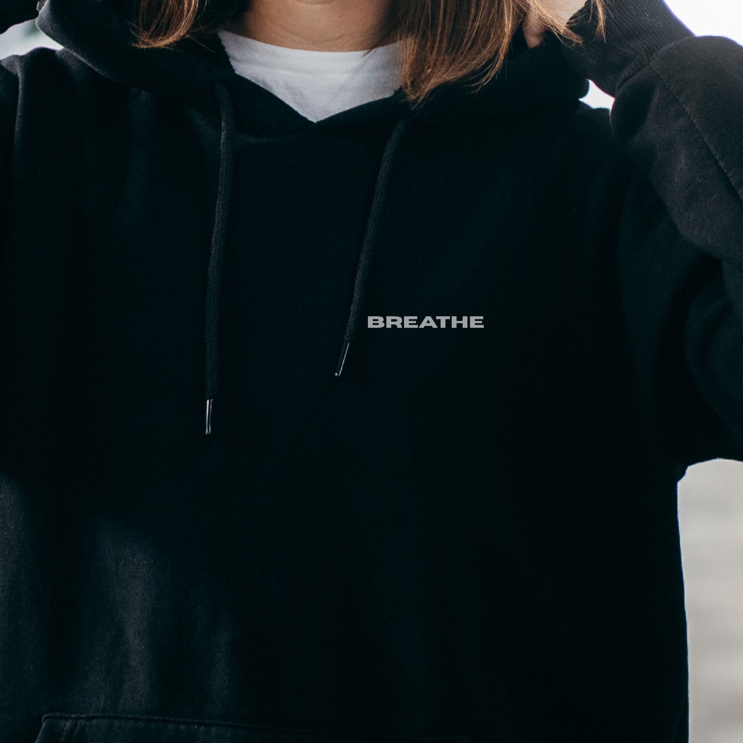 Close-up of model wearing black oversized VIKA&EVE BREATHE hoodie by the water – minimalist unisex design for who we strive to be.