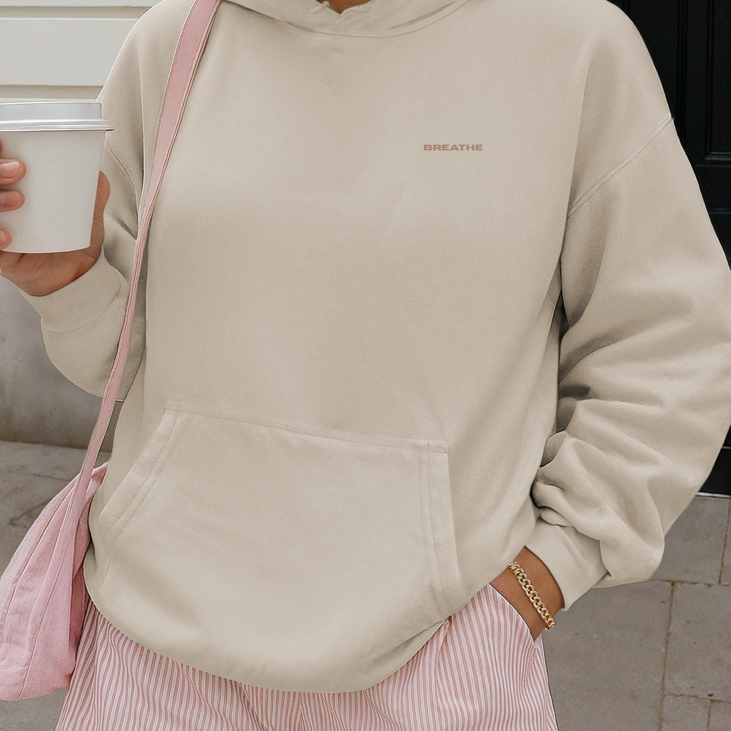 Street style model wearing sand organic Vika&Eve hoodie with coffee in hand – minimalist unisex premium comfort