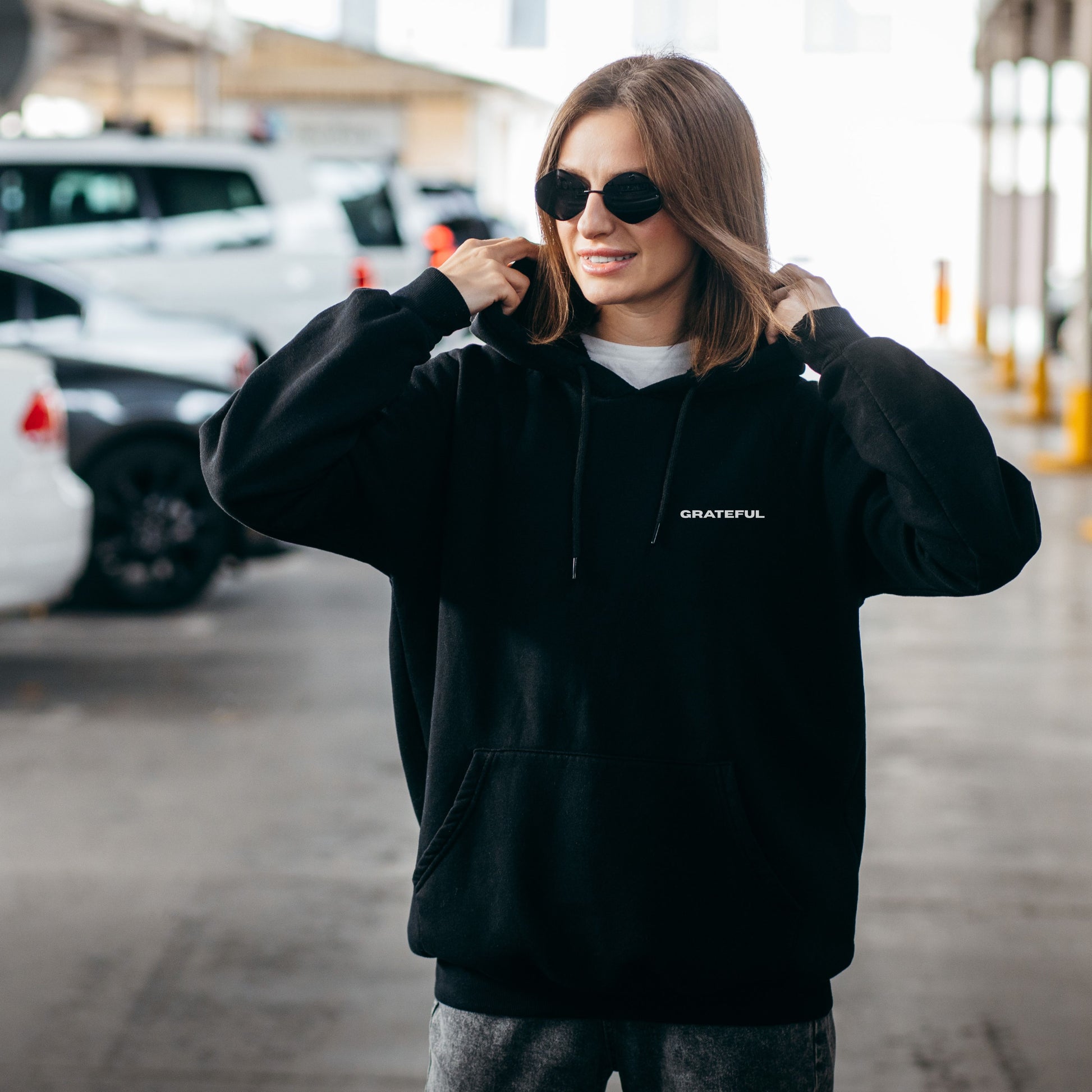 Model wearing black oversized VIKA & EVE  GRATEFUL hoodie outdoors – minimalist unisex design for who we strive to be.