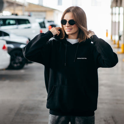 Model wearing black oversized VIKA & EVE  GRATEFUL hoodie outdoors – minimalist unisex design for who we strive to be.