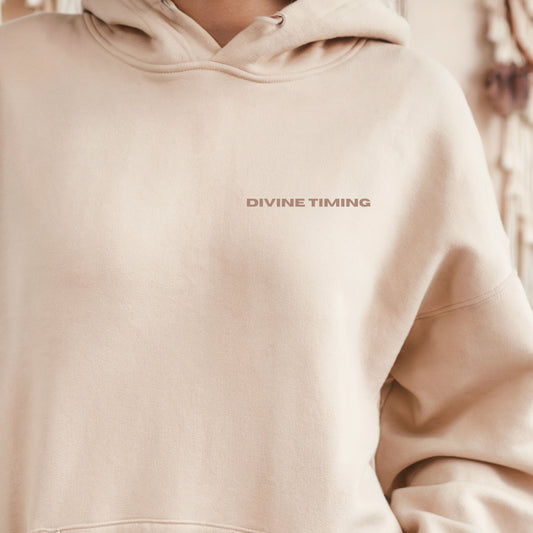Close-up of model wearing sand oversized VIKA & EVE  DIVINE TIMING hoodie by the water – minimalist unisex design for who we strive to be.