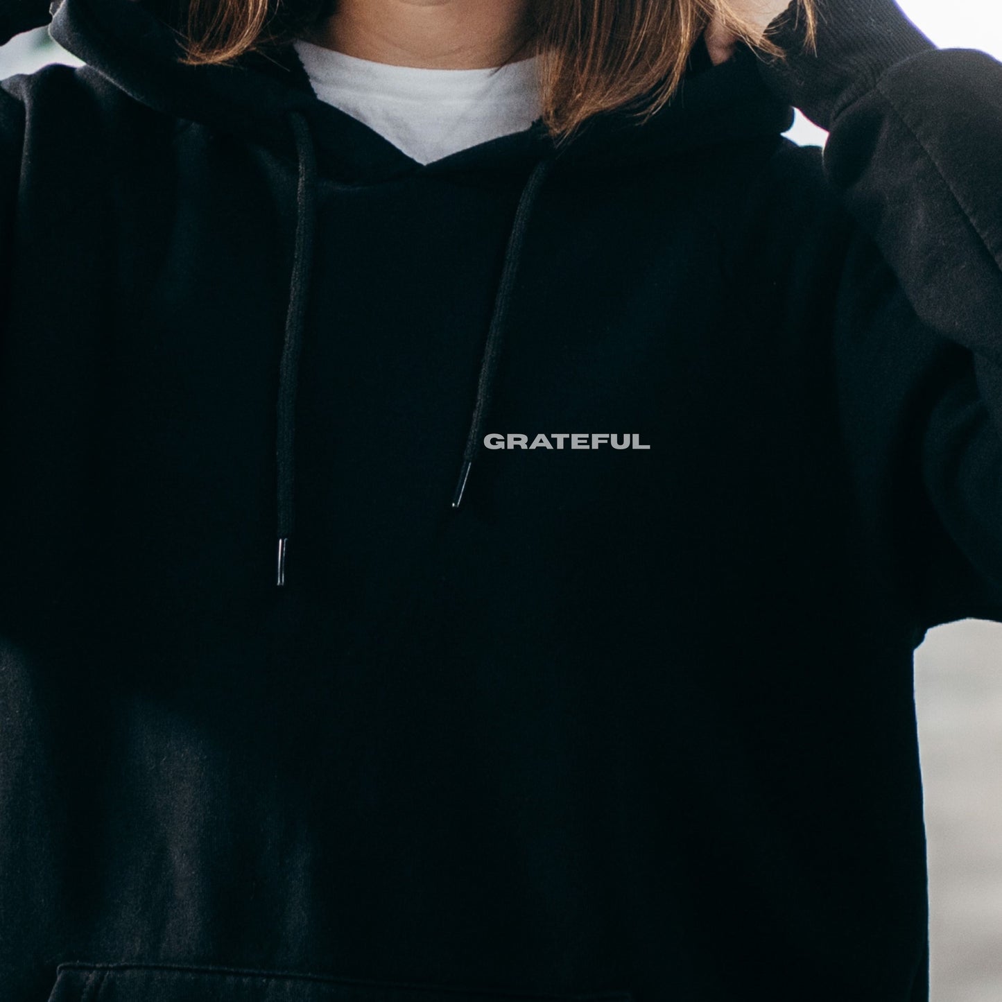 Close-up of model wearing black oversized VIKA&EVE  GRATEFUL hoodie by the water – minimalist unisex design for who we strive to be.