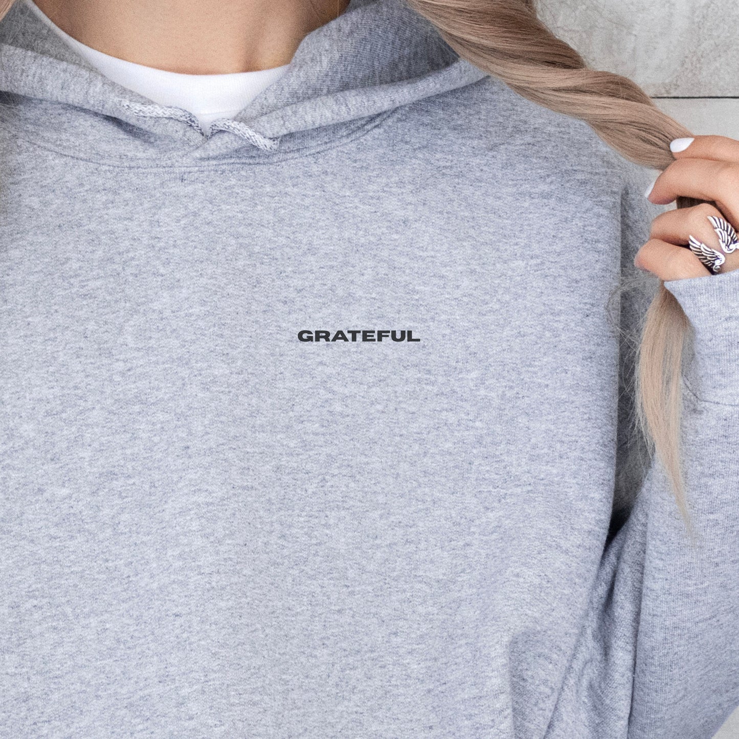 Close-up of model wearing grey oversized VIKA&EVE  GRATEFUL hoodie by the water – minimalist unisex design for who we strive to be.