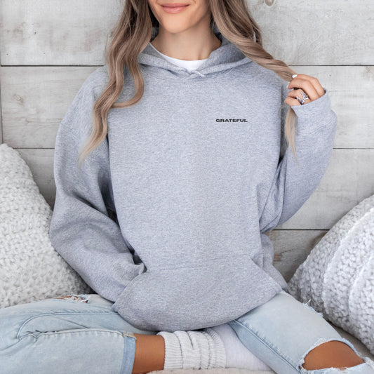 Model wearing grey oversized  GRATEFUL VIKA &E VE hoodie sitting indoors – minimalist unisex design for who we strive to be.